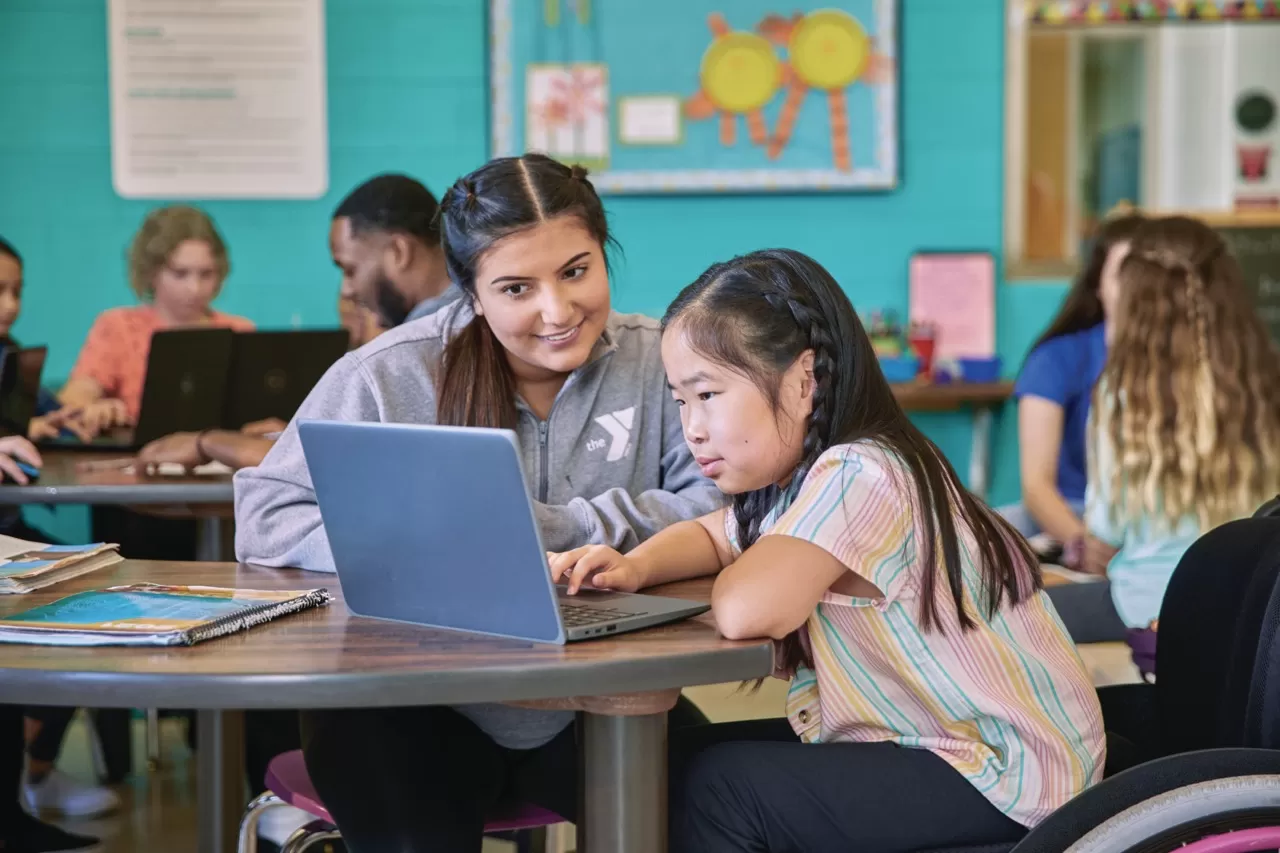 YMCA leader helping child with homework on a laptop