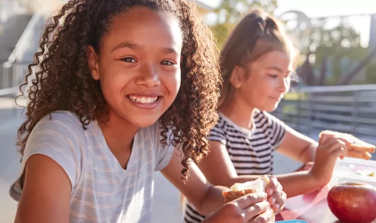 Two happy girls eating sandwiches outside