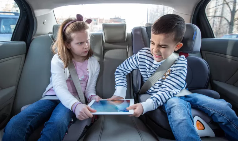 brother and sister fighting over a tablet in the backseat of a car