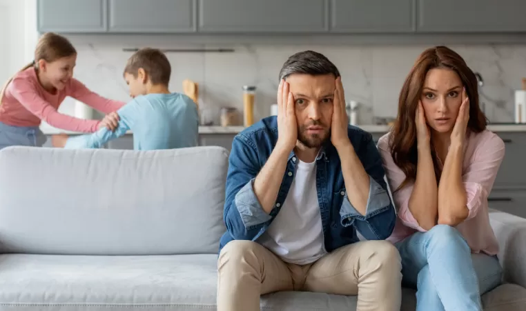 stressed out parents with kids play fighting in the background
