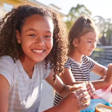 Two happy girls eating sandwiches outside