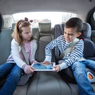 brother and sister fighting over a tablet in the backseat of a car