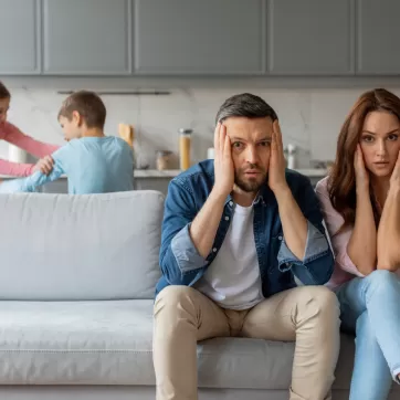 stressed out parents with kids play fighting in the background